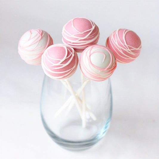 Five pink and white cake pops with drizzled candy coating displayed in a clear glass vase