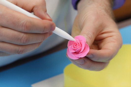 Close-up of hands shaping a small pink gumpaste rose petal with a pointed modeling tool