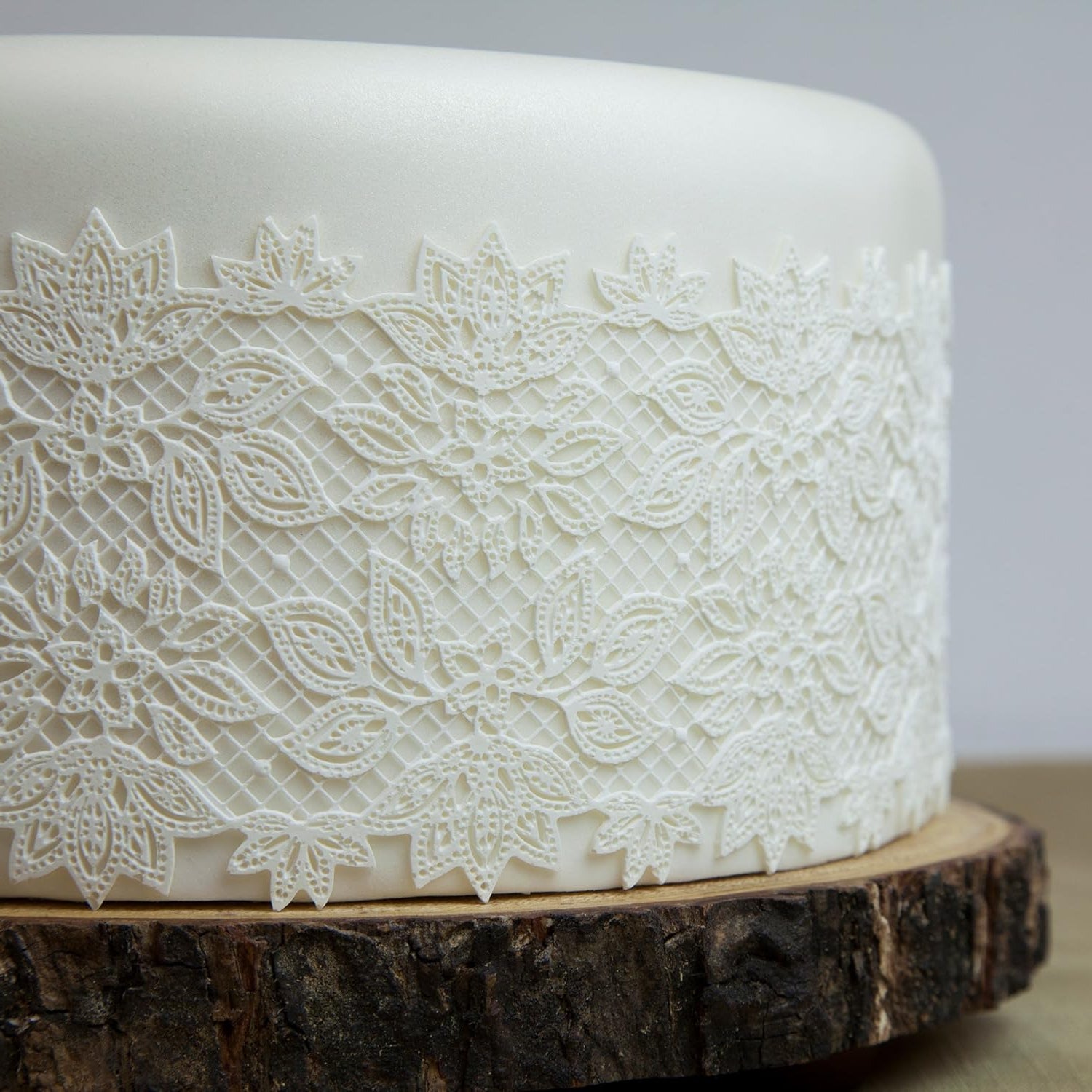 White cake with lace detailing on a wooden stand against a gray background