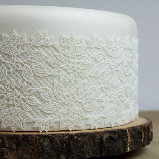White cake with lace detailing on a wooden stand against a gray background
